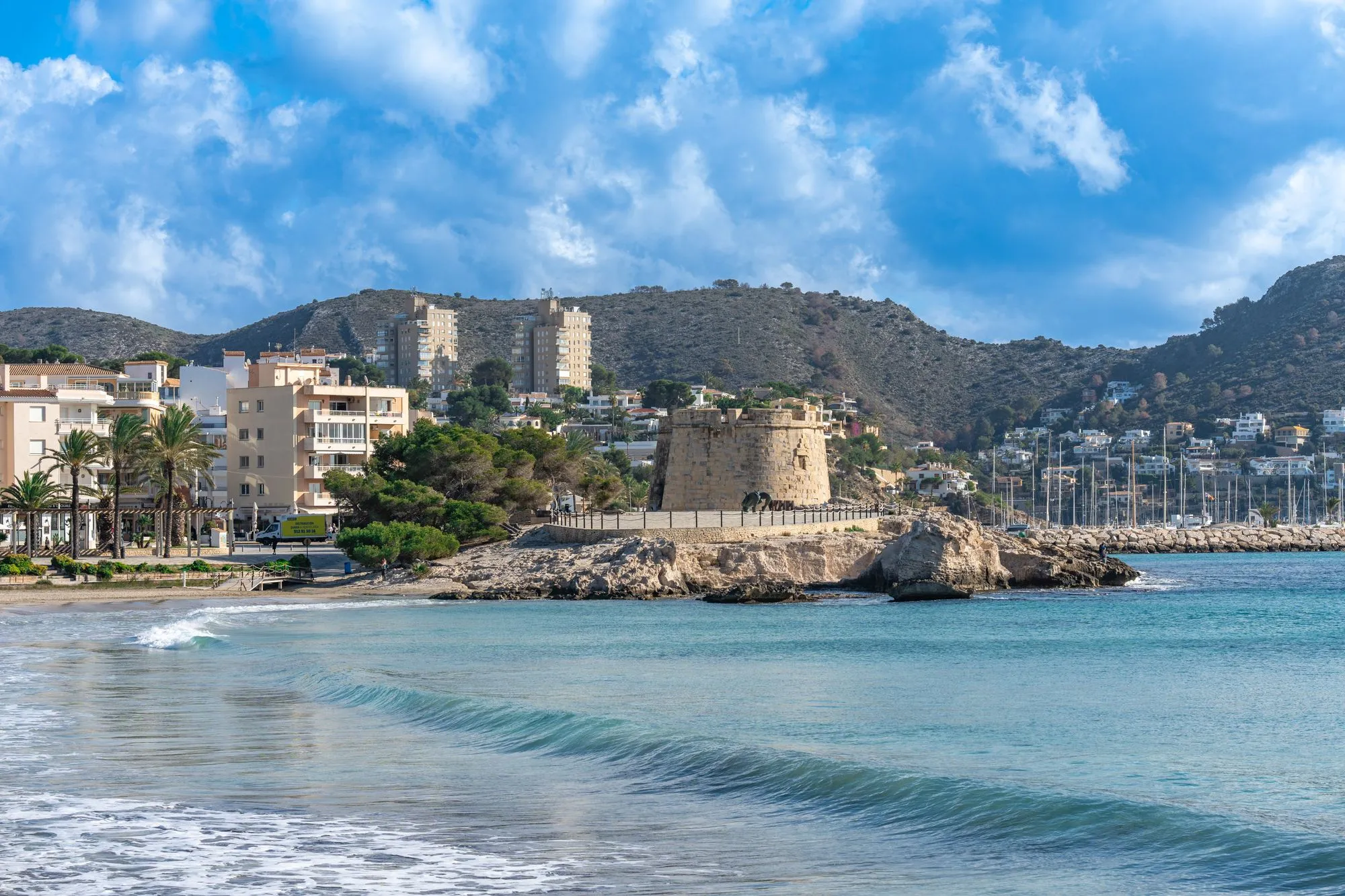 Strand van Moraira met een historische toren aan zee en de jachthaven erachter